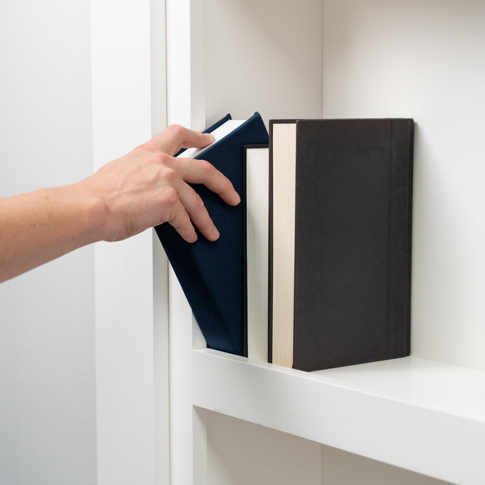 Hand reaching for a navy book on a white Murphy Door® bookshelf with black hardcover books nearby.